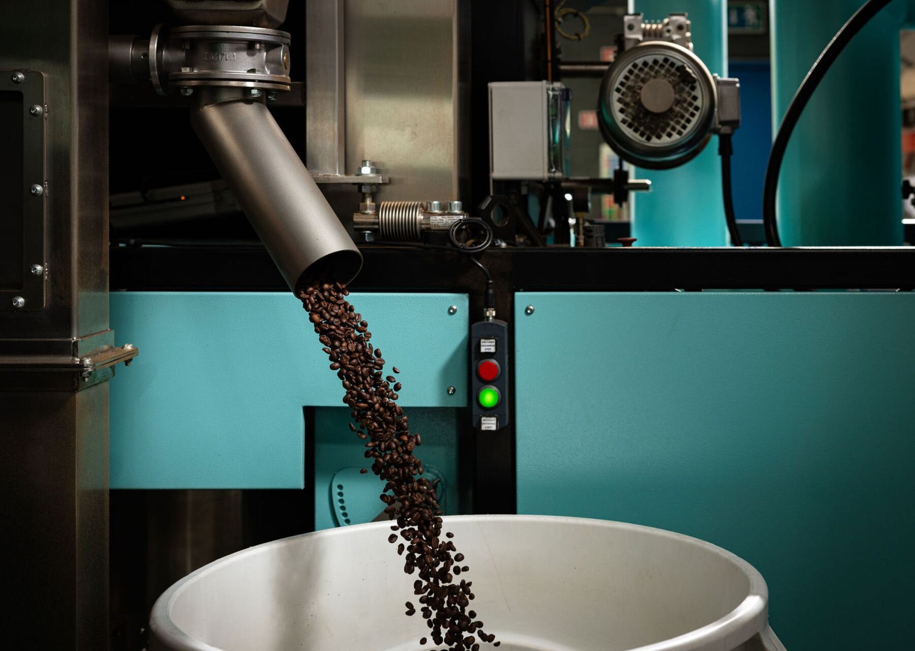 Roasted coffee beans falling from the chute of the roaster into a cooling tray